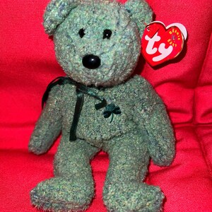 Puede incluir: Oso de peluche verde Beanie Baby con un trébol en el pecho y una etiqueta Ty unida a la oreja. El oso tiene ojos negros y una nariz negra.