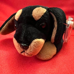 May include: A black and brown plush toy dog with floppy ears and a brown nose. The dog is lying down with its head resting on its paws.
