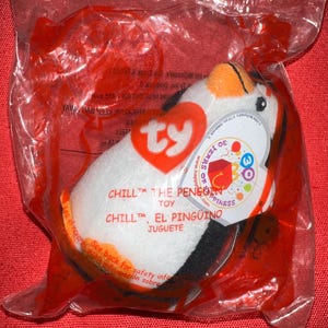 Op de afbeelding: Een TY Beanie Baby pinguïn speelgoed genaamd "Chill" in een doorzichtige plastic zak. De pinguïn is wit met zwarte, oranje en gele accenten. Het label luidt "30 Years of Happiness" en "Chill the Penguin Toy".