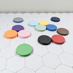 May include: Assortment of colorful round phone grips in various colors including orange, pink, green, black, red, brown, purple, blue, and yellow. The phone grips are arranged on a white hexagonal tile surface.