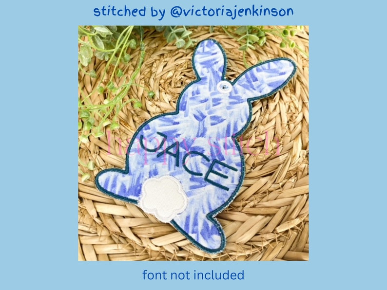 May include: A blue and white patterned bunny-shaped applique with the name "JACE" embroidered on it. The applique has a white fluffy tail and a dark blue border. Text at the top reads "stitched by @victoriajenkins", and at the bottom, "font not included".
