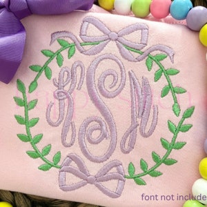 Pode incluir: Um tecido rosa com um laço roxo e um monograma com as letras "JSM" rodeado por uma coroa verde com laços. O texto "font not included" está na parte inferior da imagem.