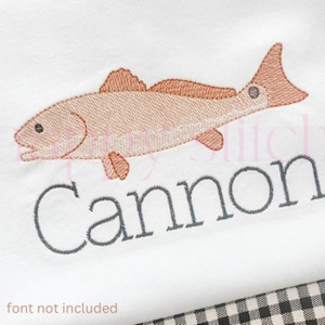May include: Embroidered design of a red fish with the name Cannon stitched underneath. The design is on a white fabric background.