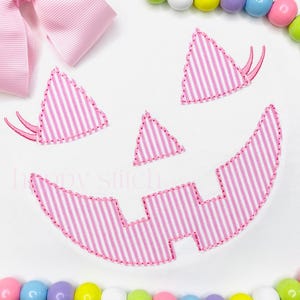 May include: A pink and white striped pumpkin face design, perfect for Halloween crafts. The design includes a large smiling mouth, triangular eyes, and a small triangle nose. A pink bow is in the upper left corner. Colorful beads surround the design.
