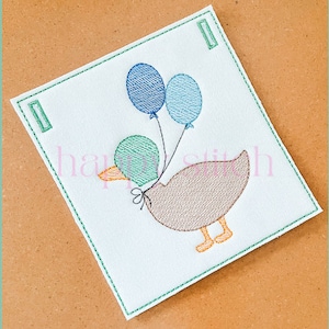 May include: Embroidered design of a brown duck holding three blue and green balloons. The duck has a yellow beak and orange feet.