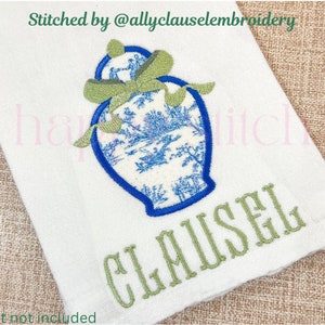 May include: White kitchen towel with blue and white embroidered design of a ginger jar with green leaves and a green ribbon. The text "CLAUSEL" is embroidered in green below the ginger jar. The text "Stitched by @allyclauselembroidery" is at the top of the towel.