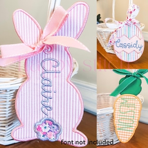 May include: Three embroidered Easter basket tags. A pink and white striped bunny tag with the name "Claire" embroidered on it. A blue and white striped egg tag with the name "Cassidy" embroidered on it. A green and orange striped carrot tag with the name "Weston" embroidered on it.