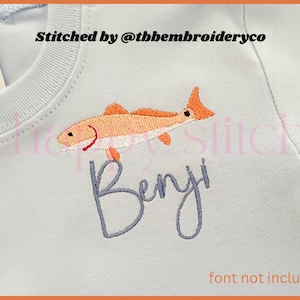 May include: A light blue t-shirt with an embroidered red fish and the name "Benji" in a cursive font. The text "Stitched by @tbhembroideryco" is also visible on the shirt. The text "font not included" is at the bottom of the image.