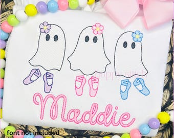 Pode incluir: Camiseta branca com três desenhos de fantasmas, cada um adornado com uma flor e sapatilhas de ballet. O nome "Maddie" é bordado em rosa abaixo. Um laço rosa e contas coloridas decoram a borda.