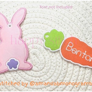 May include: A pink bunny-shaped applique with a purple tail, and a green leaf-shaped applique, next to an orange carrot applique with the name "Benton" stitched in white. The items are on a woven surface.