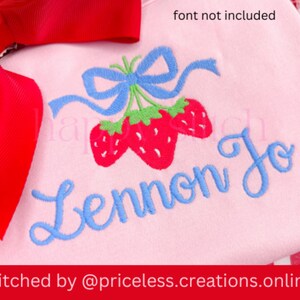 May include: Pink embroidered shirt with a blue bow and three red strawberries. The name Lennon Jo is embroidered in blue cursive lettering. "Stitched by @priceless.creations.online" is printed below the design.