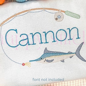 May include: Embroidered design featuring a fishing rod and a marlin. The name "Cannon" is embroidered in teal. The fishing rod is tan and green, with a fishing reel. The marlin is blue and white. Text at the bottom reads "font not included".