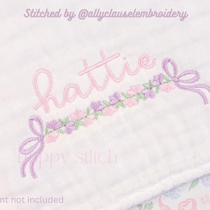 May include: Embroidered design on white fabric featuring the name "Hattie" in pink script, adorned with a floral garland in shades of pink and purple. The design includes bows on each end. Text at the top reads "Stitched by @allyclausembroidery" and at the bottom "font not included".