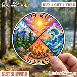 May include: A round sticker or magnet featuring a colorful design with four quadrants: mountains, sun, waves, and a campfire. The words "IN MY ELEMENT" are displayed. The sticker is held by a hand.