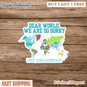 May include: A white sticker or magnet with a colorful world map and the text "DEAR WORLD, WE ARE SO SORRY. LOVE, SANE AMERICANS." The sticker has a wooden background. The text "BUY 5 GET 1 FREE" is also visible.