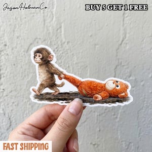 May include: A sticker featuring a brown monkey pulling an orange teddy bear. The monkey is walking, holding the bear's arm. The sticker has the text "BUY 5 GET 1 FREE" and "FAST SHIPPING". The brand name "Jason HolmanCo" is also visible.