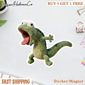May include: A green felt lizard sticker with a wide open mouth and pink tongue. The sticker has large white eyes and is in a dynamic pose. The text "BUY 5 GET 1 FREE" is at the top. The text "Sticker/Magnet" is at the bottom.
