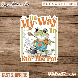 May include: A sticker featuring a cartoon frog in overalls stirring a pot with a wooden spoon. The text reads "On My Way To Stir The Pot." The sticker has a white border and is on a wooden background.