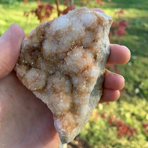 May include: A large, rough, white and brown crystal cluster with a natural, irregular shape. The crystal has a rough, textured surface and is covered in small, white crystals.