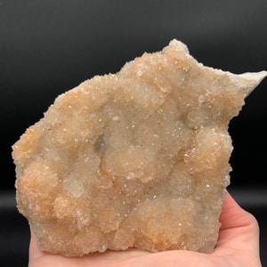 May include: A cluster of small, white and orange crystals on a rough, natural rock. The crystals are densely packed together, creating a textured surface.