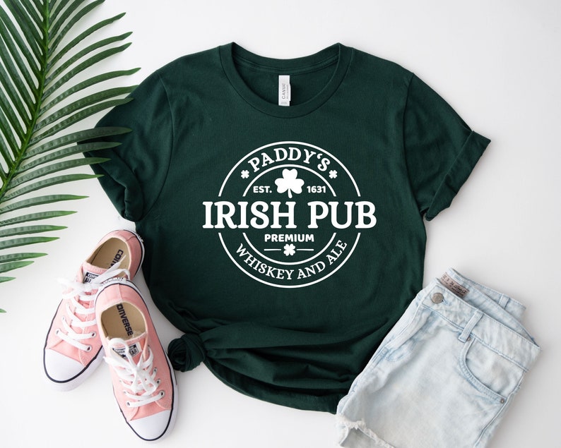 May include: A green t-shirt with a white circle design that says "Paddy's Irish Pub" with a shamrock and the text "Est. 1631" and "Premium Whiskey and Ale".