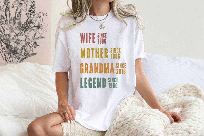 a woman sitting on a bed wearing a white t - shirt