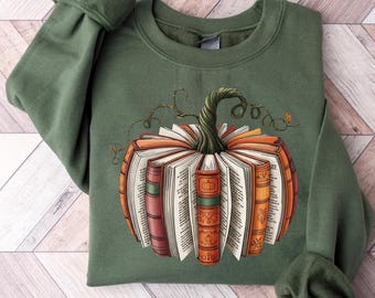 Puede incluir: Sudadera verde con un diseño de calabaza hecho de libros abiertos. La calabaza tiene un tallo verde y detalles de vid. Los libros son naranjas, rojos y marrones con páginas blancas. Un gráfico con temática otoñal para los amantes de los libros.