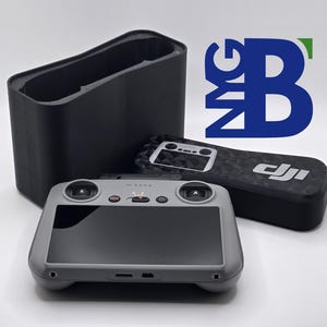 Op de afbeelding: Een grijze DJI drone-afstandsbediening met een scherm, knoppen en een DJI-logo. De afstandsbediening ligt op een zwart en grijs hoesje met een DJI-logo. De afstandsbediening ligt ook op een zwarte draagtas.
