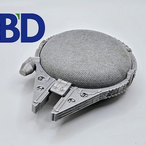May include: A silver 3D printed model of the Millennium Falcon spaceship from Star Wars. The model is detailed and has a textured surface.