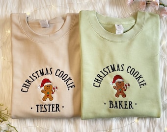 May include: Two Christmas-themed sweatshirts, one beige and one light green, with an embroidered gingerbread man and the text "Christmas Cookie" and a personalised name. The beige sweatshirt says "Tester" and the green sweatshirt says "Baker".