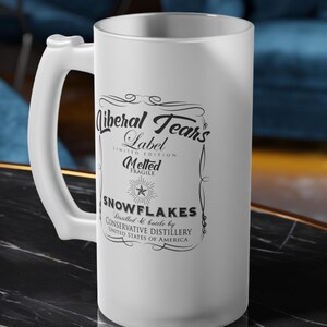 May include: A frosted glass beer stein with a large handle. The stein features a label with the text "Liberal Tears Label" and "Melted Snowflakes" in a decorative frame. The words "Conservative Distillery" are also visible.