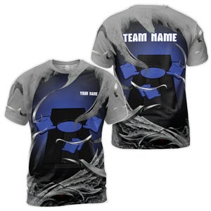 Puede incluir: Camiseta gris con un diseño azul y negro de un tablero de cornhole con bolsas. El texto "TEAM NAME" está en la parte posterior de la camiseta y "YOUR NAME" está en la parte delantera.