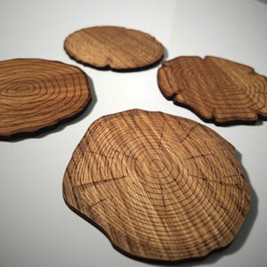 Può includere: Quattro sottobicchieri in legno con finitura in legno naturale. Ogni sottobicchiere presenta un design circolare con anelli concentrici, che ricordano la sezione trasversale di un tronco d'albero.