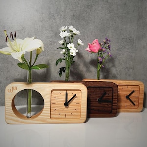 Puede incluir: Tres juegos de reloj y jarrón de madera con diferentes acabados de madera. Los relojes tienen manecillas negras y marcas de números romanos. Los jarrones son tubos de ensayo de vidrio transparente. Los juegos están dispuestos en una fila sobre una superficie marrón claro.