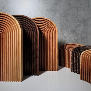 Puede incluir: Cinco arcos de madera de diferentes tamaños, apilados en una fila. Los arcos están hechos de finas piezas de madera curvadas, creando un efecto de capas. Los arcos son de color marrón, siendo los dos más grandes de madera más clara y los tres más pequeños de madera más oscura.