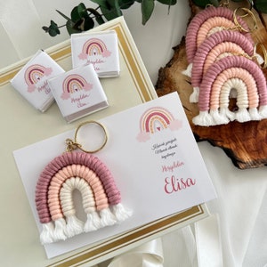 May include: A pink and white rainbow keychain with a gold ring. The keychain is on a white card with the text "Kırmızı gökyüzüyle Maviçik ellere bağışlanmış" and "Hoşgeldin Elisa".