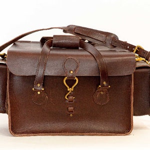 May include: A brown leather travel bag with two side pockets and a brass buckle closure.