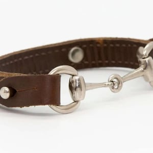 May include: A brown leather bracelet with a silver horse bit clasp.