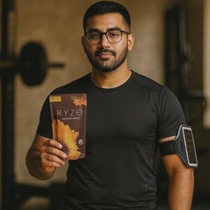 Pu&ograve; includere: Una busta marrone di caff&egrave; ai funghi Ryze con un grafico a girasole, tenuta da una persona che indossa una maglietta sportiva nera a maniche corte e una fascia da braccio per smartphone. Il testo sopra recita: Power Your Workout Without the Crash.