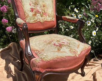 May include: A vintage armchair with a carved wooden frame and floral upholstery. The chair has a high back and curved arms. The upholstery is a pink and cream floral pattern.