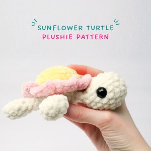 Puede incluir: Un juguete de peluche de tortuga girasol tejido a crochet con una concha amarilla y rosa. El juguete está siendo sostenido en una mano.