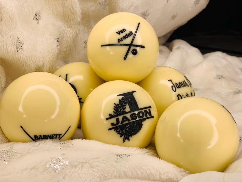 May include: Six white billiard balls with black personalized text. The balls are arranged in a pyramid shape. The text on the balls includes "Van Arsdell", "Jason", "James Dittrich", and "Barnett".