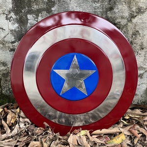 Op de afbeelding: Een rood, wit en blauw Captain America schild met een zilveren ster in het midden. Het schild is gemaakt van metaal en heeft een glanzende afwerking.