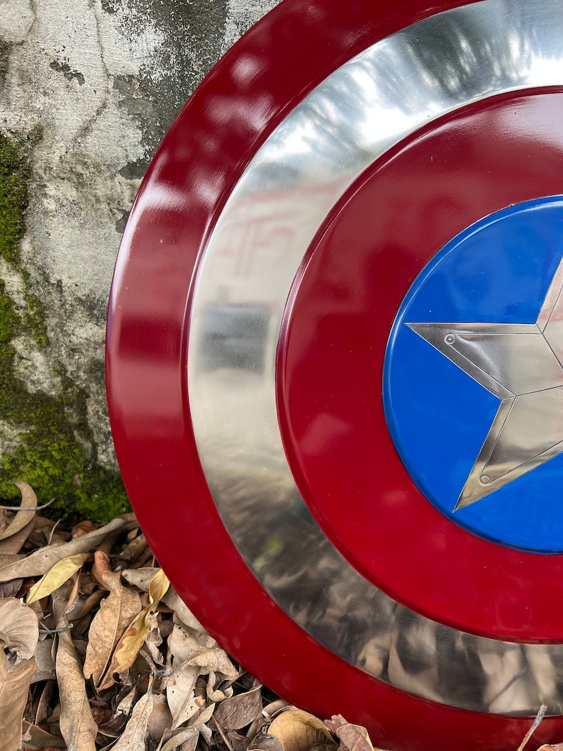 Op de afbeelding: Een rood, wit en blauw Captain America-schild met een zilveren metalen rand. Het schild ligt op een bed van bruine bladeren.
