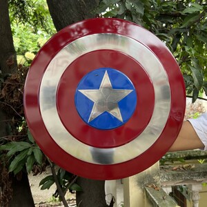 Op de afbeelding: Een rood, wit en blauw Captain America schild met een zilveren ster in het midden. Het schild is gemaakt van metaal en heeft een glanzende afwerking.