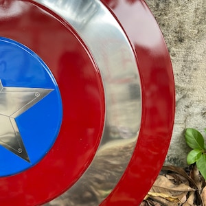 Op de afbeelding: Een rood, wit en blauw Captain America schild met een zilveren metalen rand. Het schild is gemaakt van metaal en heeft een ster in het midden.