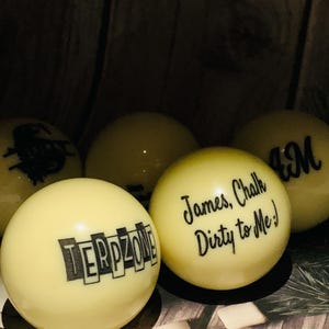 May include: Six yellow billiard balls with black lettering. The balls are arranged in a semi-circle. The text on the balls reads "TERPZONE", "James, Chalk Dirty to Me!" and "BM".