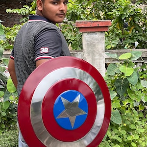 Op de afbeelding: Een persoon die een rood, wit en blauw Captain America schild vasthoudt. Het schild heeft een grote, vijfpuntige ster in het midden.
