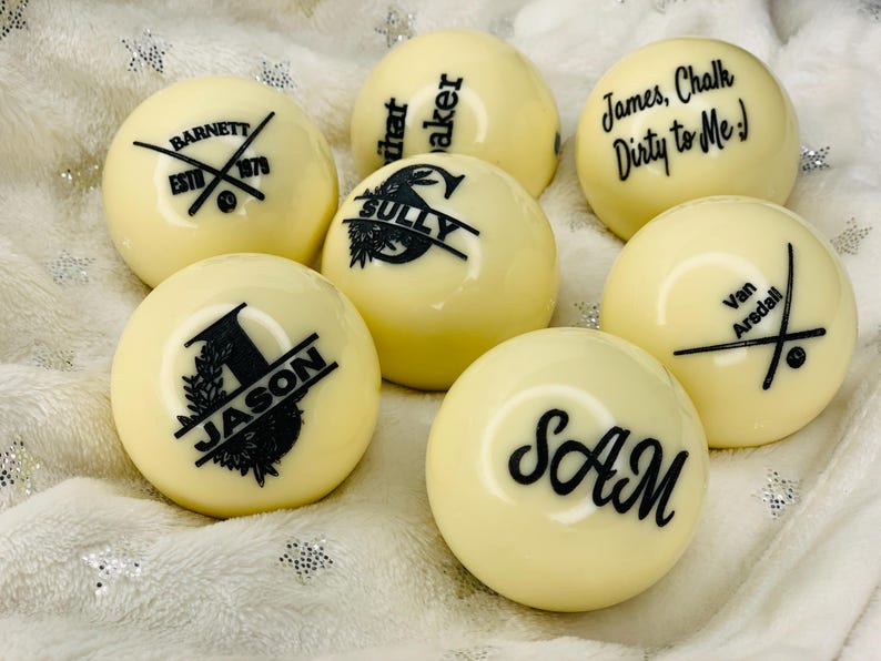 May include: Six white billiard balls with black personalized text. The text on the balls includes names, a company logo, and a funny saying.
