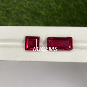 Puede incluir: Dos piedras preciosas de rubí rojo, una cuadrada y otra rectangular, sobre una superficie blanca. El texto "MJGEMS" es visible debajo de las piedras preciosas.